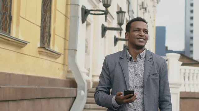 Slow-motion of young happy businessman using smartphone and looking around street outdoors