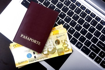 Passport and Philippine peso bills on a laptop computer.