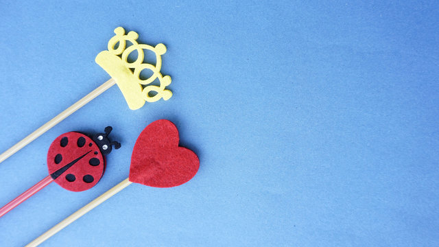 Top or flat lay view of Photo booth props a ladybird, a red heart shape and a yellow crown on a blue background flat lay. Birthday parties and weddings.