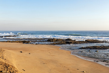 Beach Against Rocky Ocean Shoreline and Blue Sky Landscape
