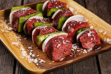 
Uncooked beef kebabs with vegetables and spices on wooden board