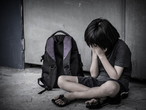 Retro picture with grain. Sad Kid sitting on the floor with school bag waiting for parent.