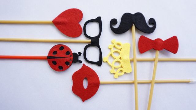 Top or flat lay view of Photo booth props a black mustache a black glases, a red bow tie, a ladybird, a red heart shape, a red lips and a yellow crown on a white isolated background flat lay. Birthday