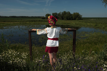  Woman girl in folk shirt embroidered dress in flowers stands near lake pond in summer
