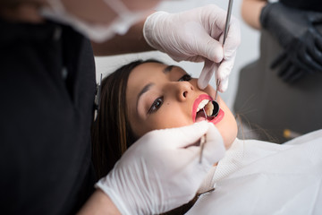 Close up of beautiful young woman having dental check up in dental clinic. Dentist examining a...