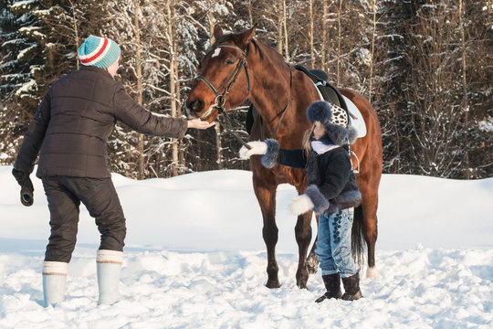 Small girl, horse trainer and horse in a winter