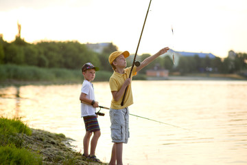 Two boys are fishing on the beach at sunset