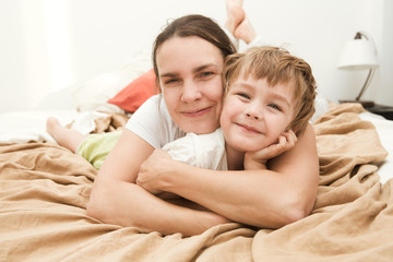 Fototapeta na wymiar mother with her little son relaxing and playing in the bed at the weekend together, lazy morning. 