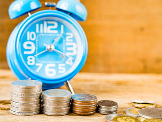 Stack of coins and alarm clock on wooden background. Business Finance and time of money concept.