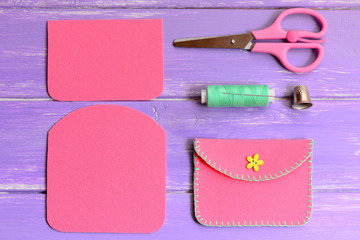 Obraz premium Children pink felt purse with yellow flower wooden button. Scissors, thread, needle, thimble on a wooden table. Easy homemade DIY made of felt. Top view