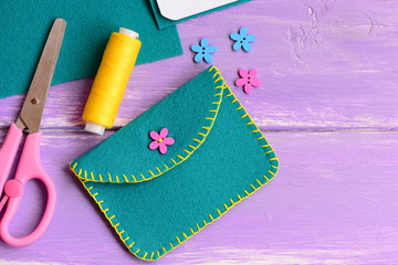 Obraz premium Small felt purse with flower wooden button. Scissors, thread, flower wooden button on a wooden background with copy space for text. Hand sewing for kids