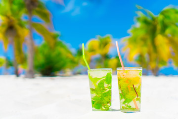 Two cold tasty mohito cocktails on the white sandy beach in palm grove