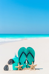 Suncream bottle, flip flops, starfish and sunglasses on white sand beach background ocean