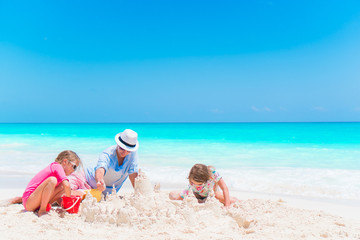 Father and little daughters making sand castle at tropical beach