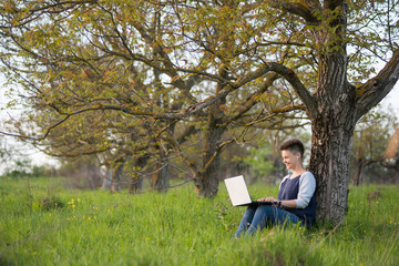 Full length shot of a happy young woman sitting under the tree in the park using her laptop positivity working studying education relaxation weekend internet online