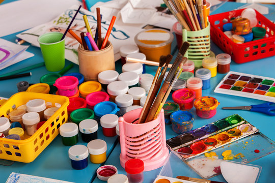Kindergarten tables with painting brush . Preschool class waiting kids. Playroom with lot object on table. Art room for children creativity. Top view still life. Materials for creative handwork.