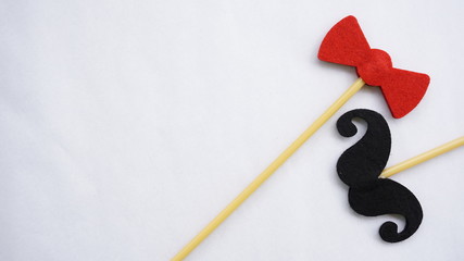 Top or flat lay view of Photo booth props red bow tie and a black mustache on a white background flat lay. Birthday parties and weddings.