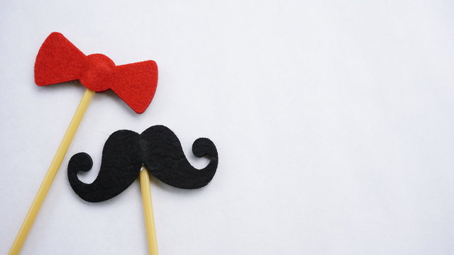 Top or flat lay view of Photo booth props red bow tie and a black mustache on a white background flat lay. Birthday parties and weddings.