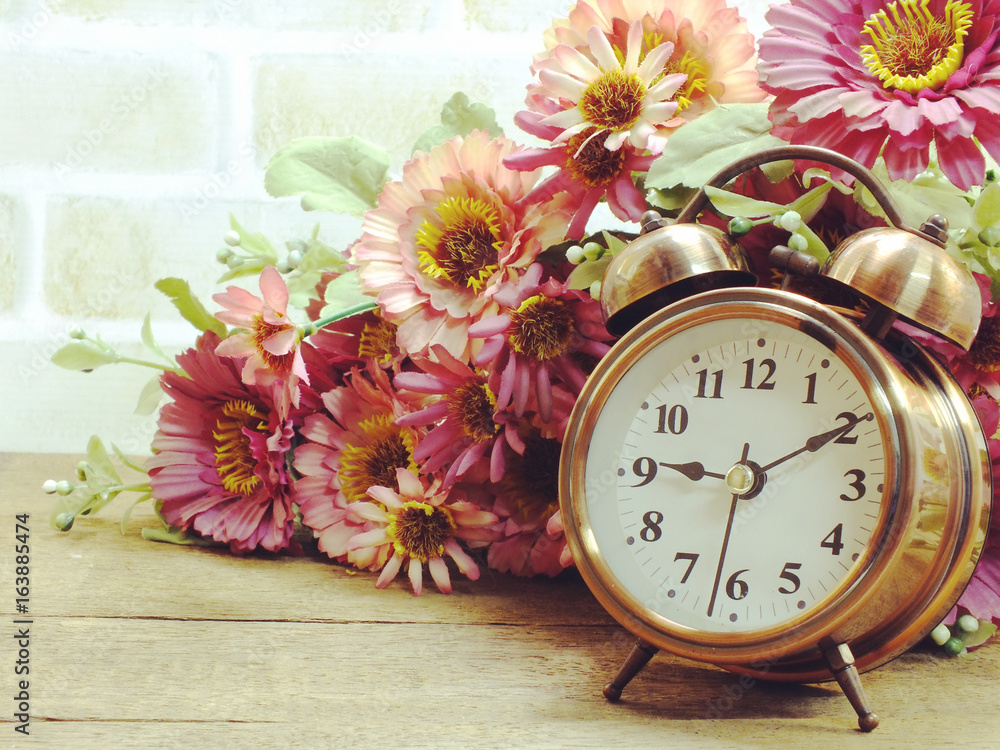 Poster spring time with alarm clock and artificial flowers bouquet background