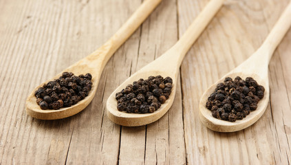 Black pepper in wooden spoon on the old board