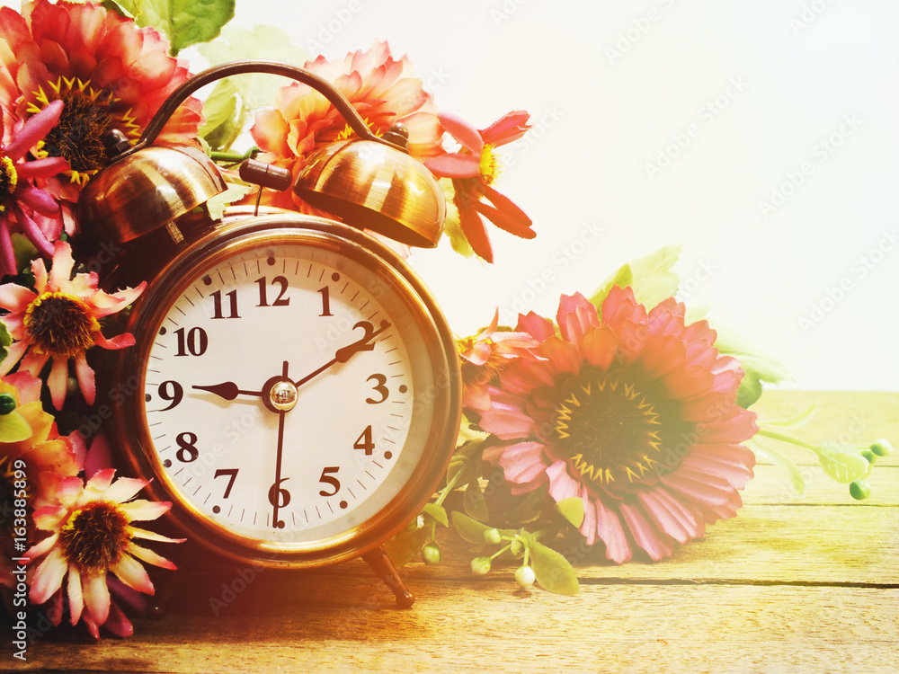 Poster spring time with alarm clock and artificial flowers bouquet background