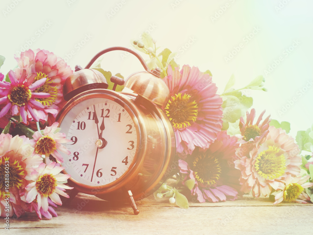 Poster spring time with alarm clock and artificial flowers bouquet background