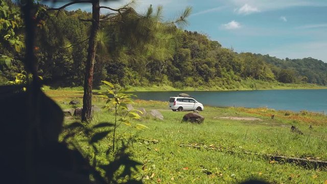 Camper van driving to a lake surrounded by hills, slide from bushes