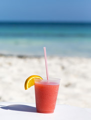 Fresh cocktail with a straw against the turquoise waters. White sand beach with isolated drink.