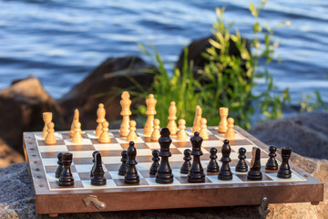 Chess board with chess pieces on rock with river embankment background