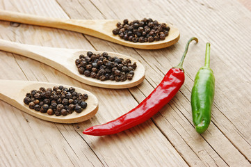 Black and red pepper in wooden spoon on the old board