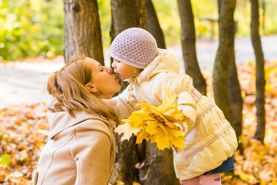 Mother kissing her daughter in the park. Woman with child on autumn forest