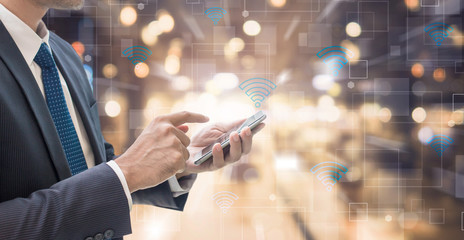 Business man using smart phone with wifi icon on blurred interior office space background - futuristic technology connection concept - obrazy, fototapety, plakaty