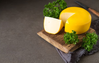 Round gouda cheese with parsley. Dark background.