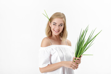 Naklejka premium smiling blond woman in white blouse holding green onion on white background. Health and vitamins