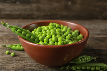 Bowl with fresh green peas on wooden background