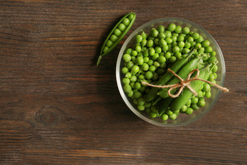Glass bowl with fresh green peas on wooden background
