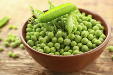 Bowl with fresh green peas on wooden background