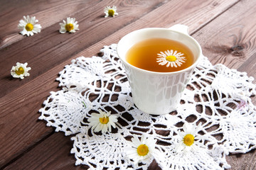 Chamomile tea on a white lacy napkin on a dark wooden background