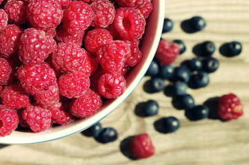 Juicy berries of raspberry in a bowl on a wooden surface, close up, top view