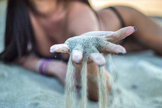 Close up view of a sensual woman's hands with sand falling through her fingers.