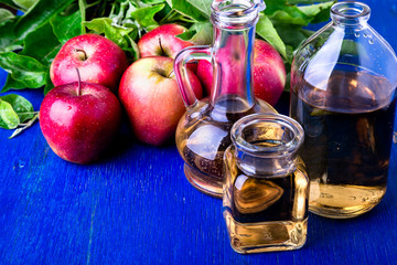 Apple cider vinegar. Three glass bottle on blue background. Red apples.