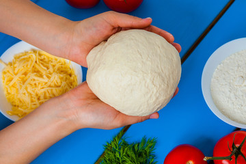 Girl holding a pizza dough, on the background of the ingredients. The chef prepares pastry.