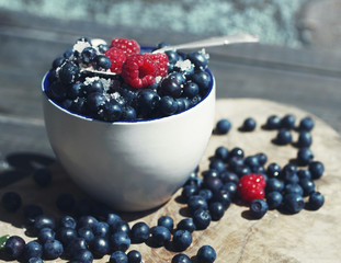 Juicy berries of bilberry and raspberry in a cup on a wooden surface, close up