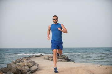 Fototapeta na wymiar Handsome bearded boy athlete sportsman jogging along stone beach