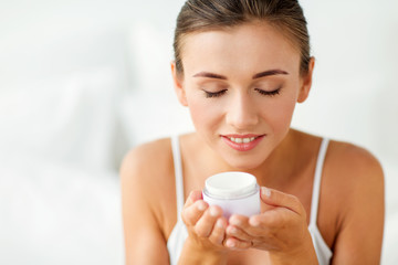 close up of happy woman holding and smelling cream