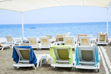 White plastic sunbeds in sandy beach under big parasol