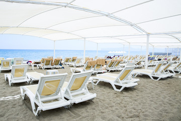 White plastic sunbeds in sandy beach under big parasol