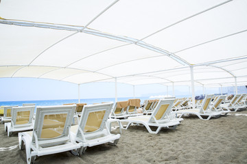 White plastic sunbeds in sandy beach under big parasol