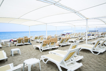 White plastic sunbeds in sandy beach under big parasol
