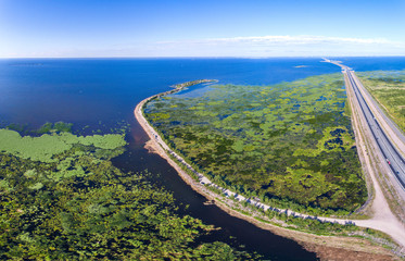 Aerial view to the road going on a reservoir of overgrown reeds and duckweed 